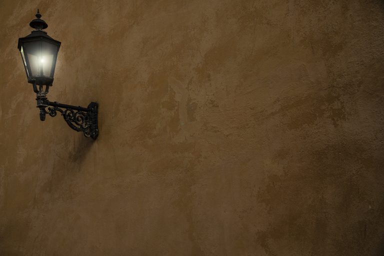 Brun vägg med grov textur och en gammeldags lysande lykta i metall upphängd